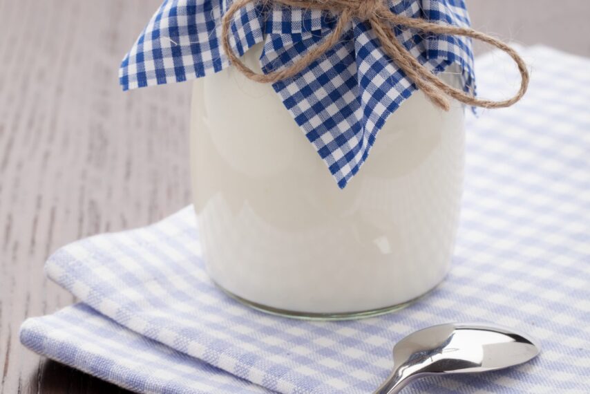 Homemade milk yogurt in glass pot and spoon on table